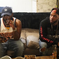 two men sitting on a couch with a cell phone