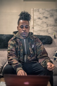 a man with dreadlocks sitting on a couch with a laptop
