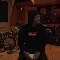 a man in a black hoodie sitting on a chair in a recording studio
