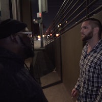 two men standing next to each other on a sidewalk at night