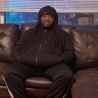 a man sitting on a couch with dreadlocks